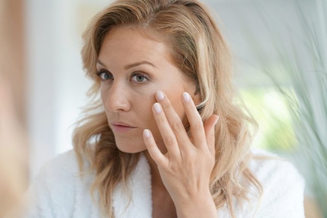 Middle-aged woman applying anti-aging creams to smooth fine lines.