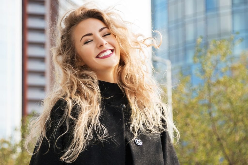 Blond woman smiling in the sun, showing off her thick full hair