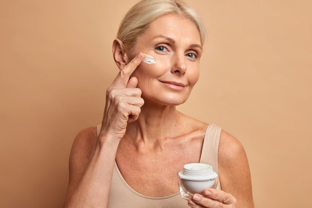 Middle aged woman applying anti-aging cream on her cheek